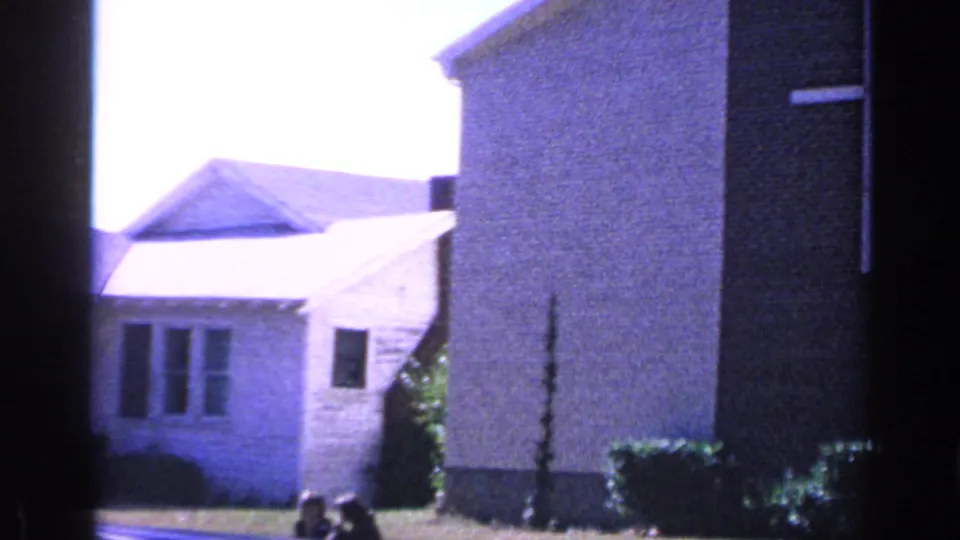 Florida church exterior seen from a residential angle, with pale walls, windows, lawn, and part of a larger brick structure.