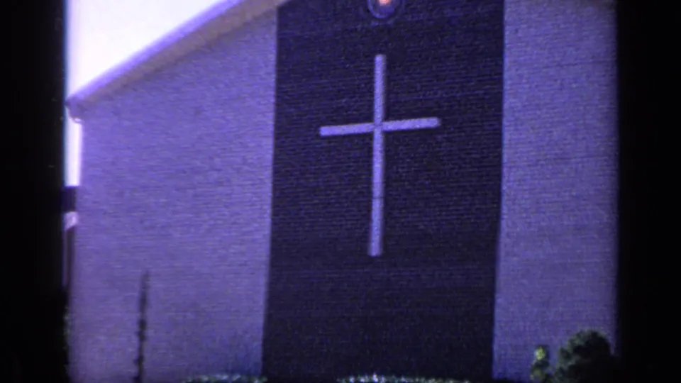 1968 Florida 8mm frame of a church facade centered on a large white cross against a dark brick vertical panel.
