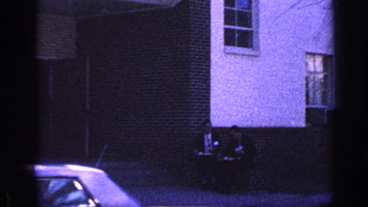 White building exterior with brick section, windows, and part of a parked car at lower left.