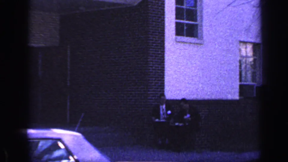 1968 Florida home-movie frame showing a white house with brick accents, upper windows, and part of a light-colored car near the street.