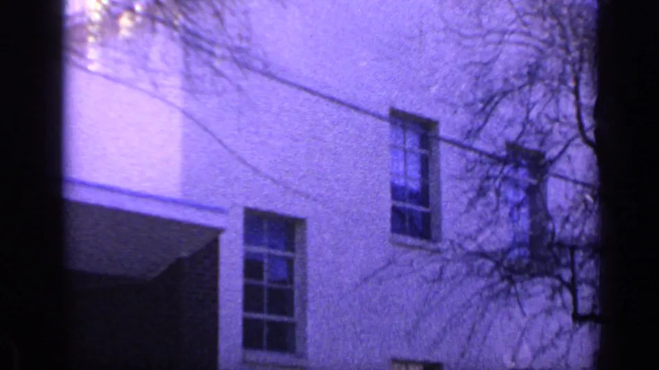 1968 Florida exterior view of a white building facade with sash windows, a recessed entry or side area, overhead line, and bare branches.