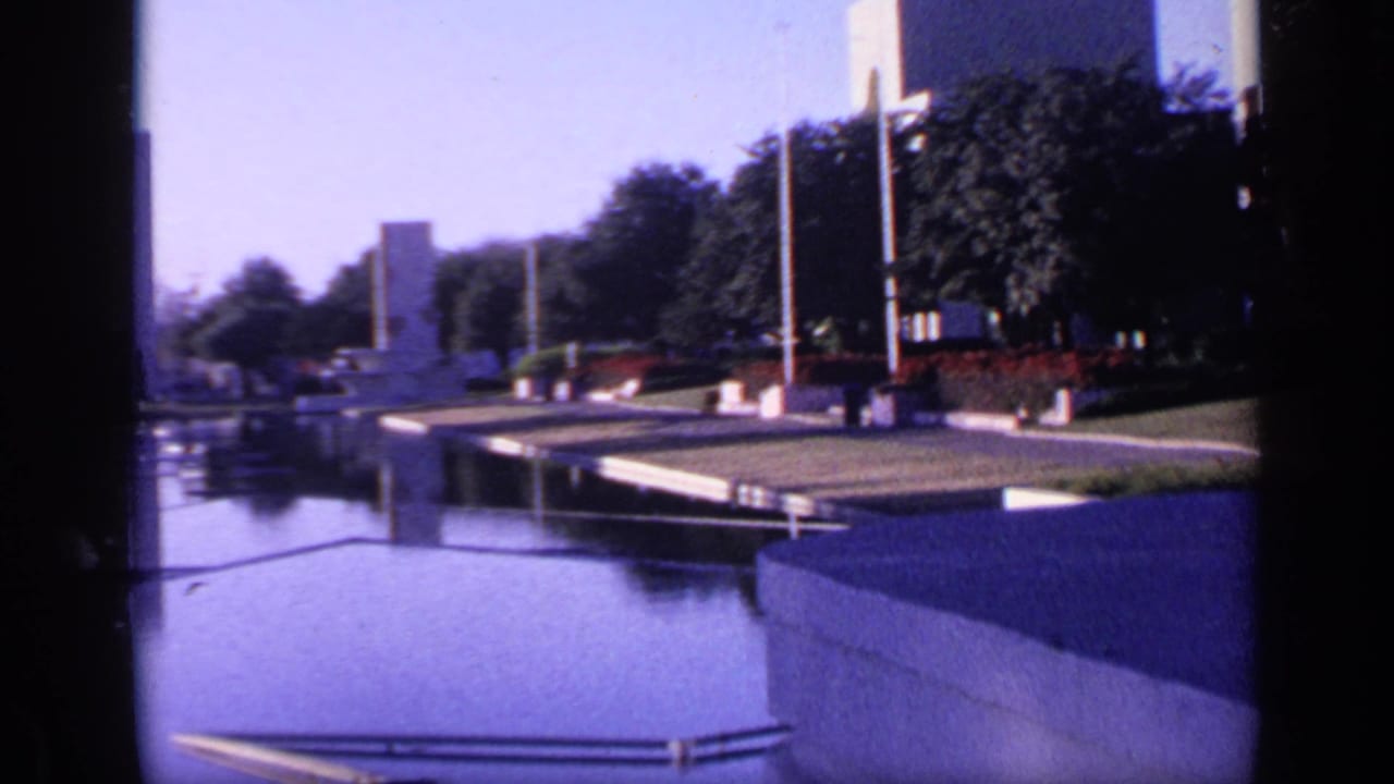 Reflective pool with tall monuments, trees, walkways, and railings in a landscaped park.