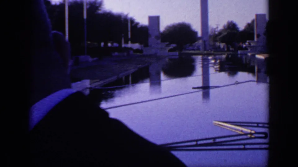 1968 Florida 8mm frame with a suited adult man partly visible in the foreground as the camera faces a reflective pool and memorial-like monuments.