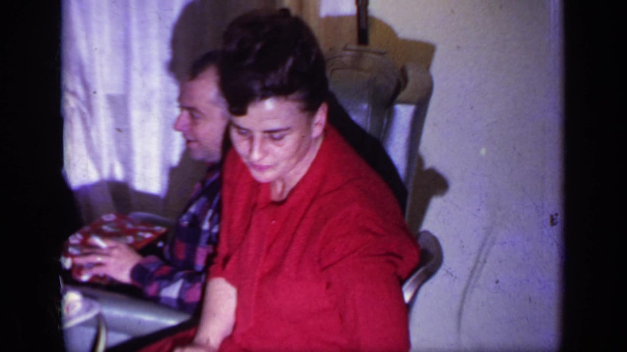 Woman in a red dress seated beside a partly visible man in a plaid shirt indoors.
