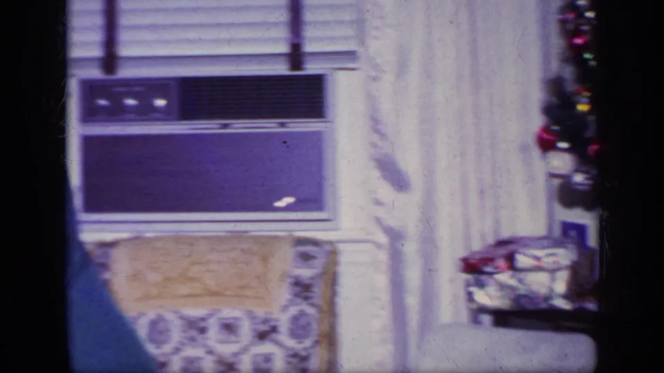 A living room view shows a window air conditioner, blinds, curtains, an upholstered chair, and holiday items near the edge of frame.