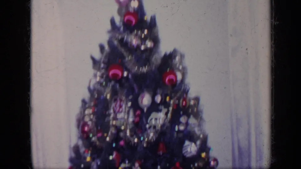 The frame centers on a Christmas tree decorated with red ornaments, tinsel, hanging decorations, and a light-colored wall behind it.