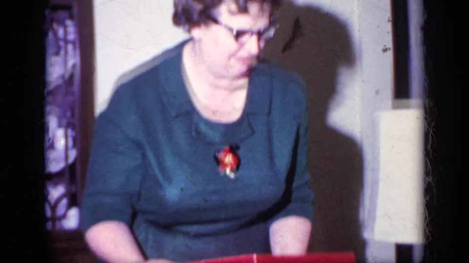 The woman leans forward over a red gift box, with a table lamp and home furnishings visible in the 1969 interior frame.