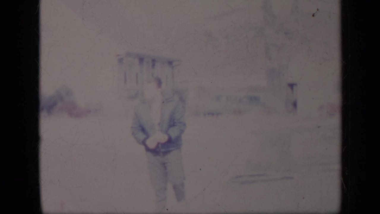 Man standing or walking near a light-colored classic car in faded 8mm footage.