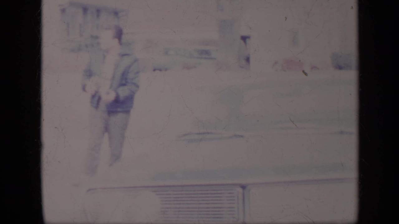 Man walking beside a light-colored classic car, with car body details visible.