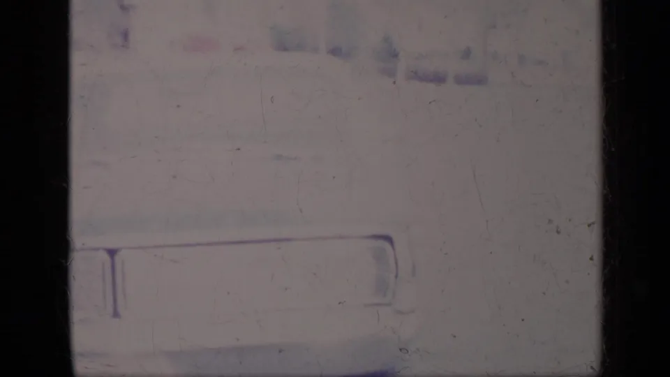 The frame centers on the light-colored car's front or rear end, while the man remains faintly visible in the washed-out upper area.