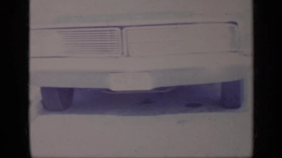 A close, faded 8mm view shows the classic car's grille, bumper, license plate area, and lower body with heavy exposure loss.