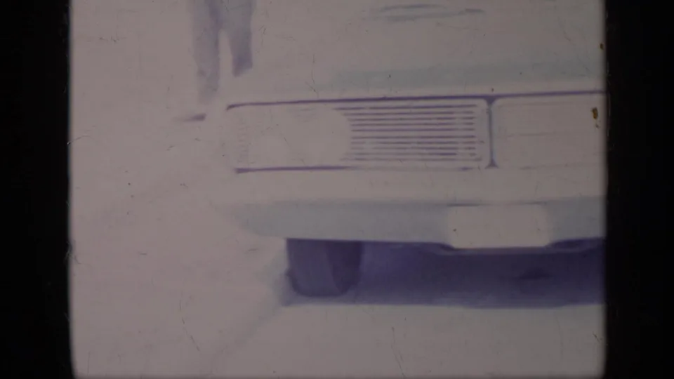 Faded 1969 8mm frame showing the rear grille and bumper area of a parked car on a bright California street.