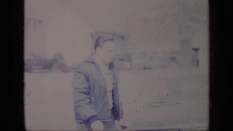 The man is seen from the side as he walks past the car in a bright residential driveway setting.