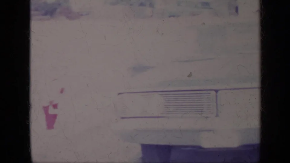 1969 California 8mm frame with the front of a white car and a small pink garment-like shape beside it, softened by film aging.