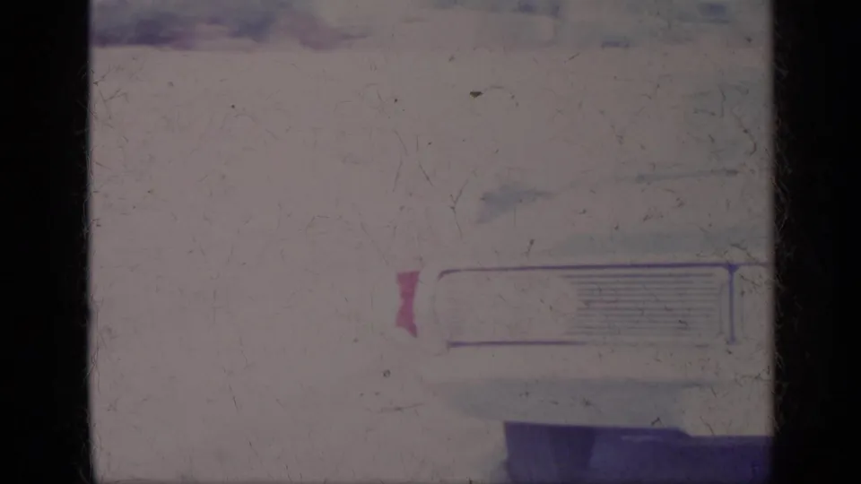 1969 California 8mm frame showing a close view of a white car front, grille detail and a small pink shape near the left edge.