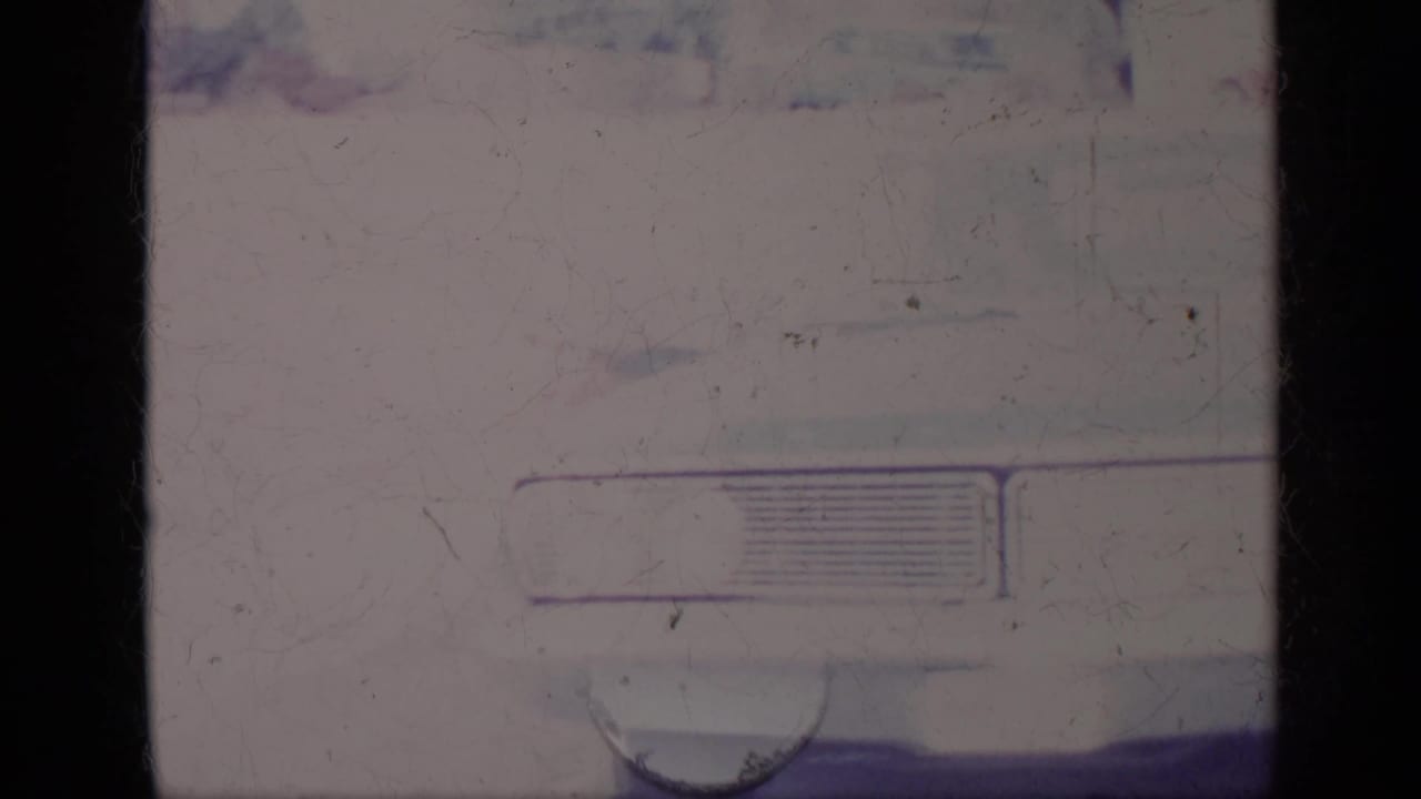 Close view of a pale classic car front corner with grille and headlight area partly visible.