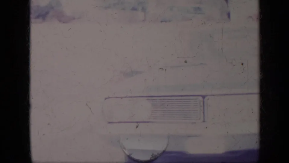 1969 California home-movie frame showing the front corner of a parked American car, with grille detail, soft focus and film scratches.