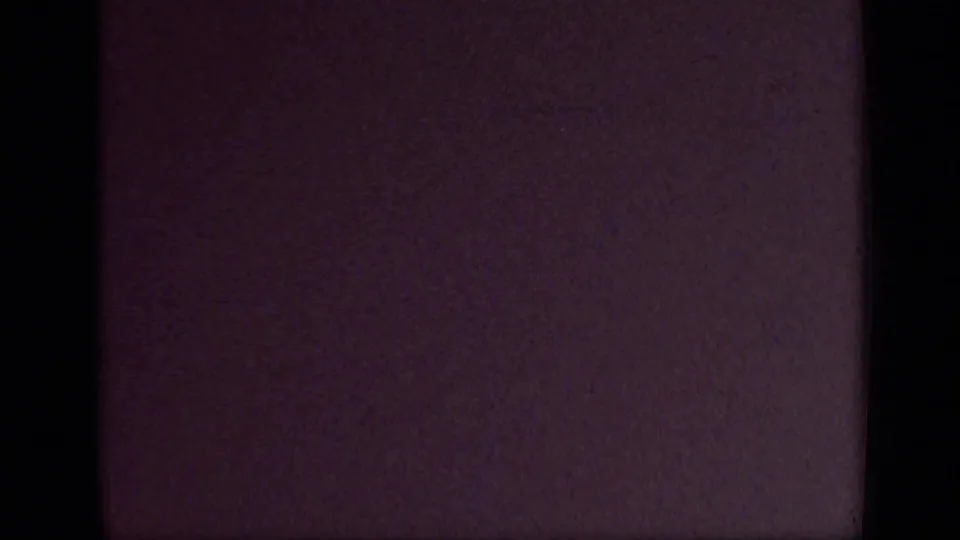 Dark, underexposed 8mm frame with a purplish cast, grain and a vertical film edge, likely from a covered camera or reel transition.