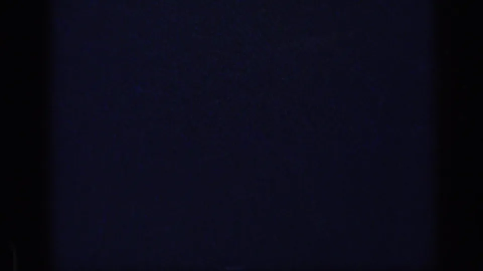 Underexposed 8mm frame showing blue-black tone, faint vertical banding and grain during a brief transition in the reel.
