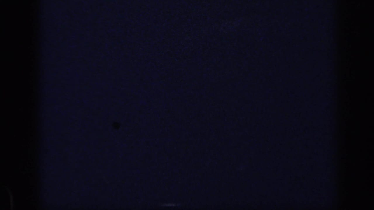 Mostly dark film frame with a partial view of adults seated at a table on the right.