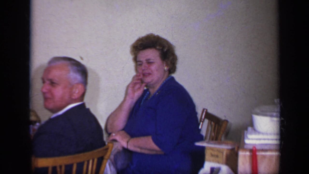 Man in a dark suit and woman in a blue dress seated at a table indoors.