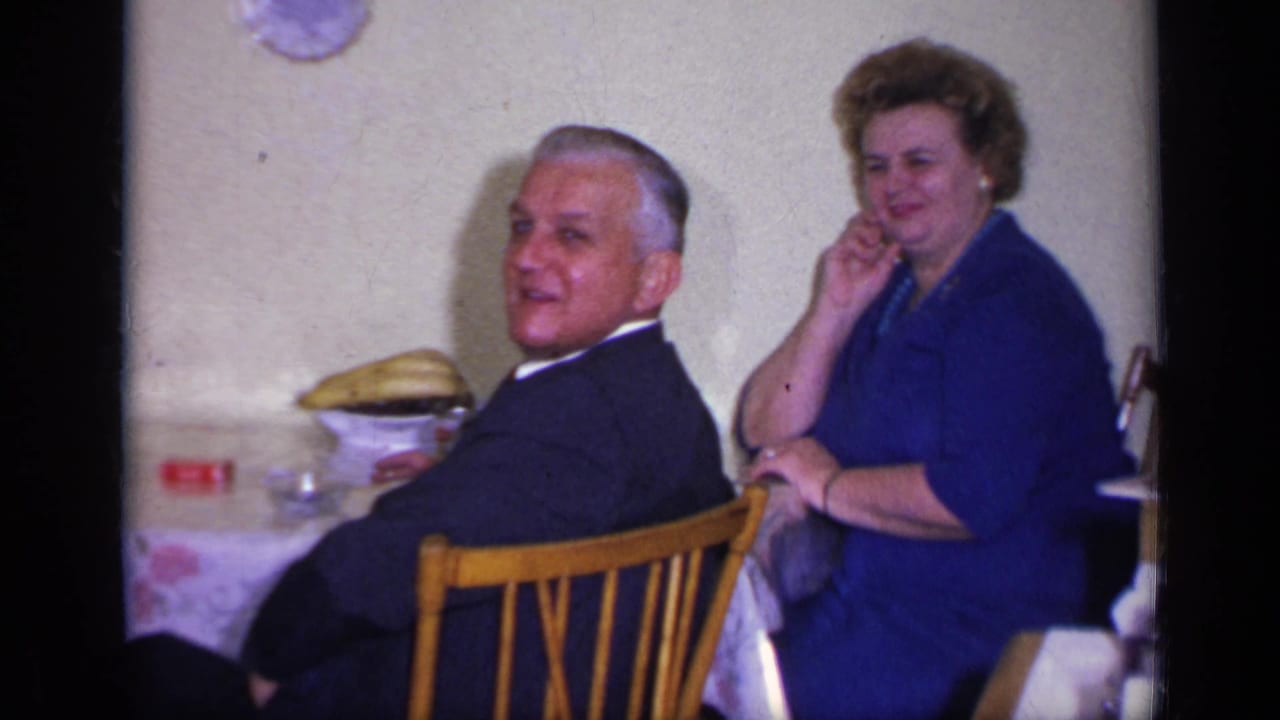 Seated man and woman look toward the camera beside a table with dishes and bananas.