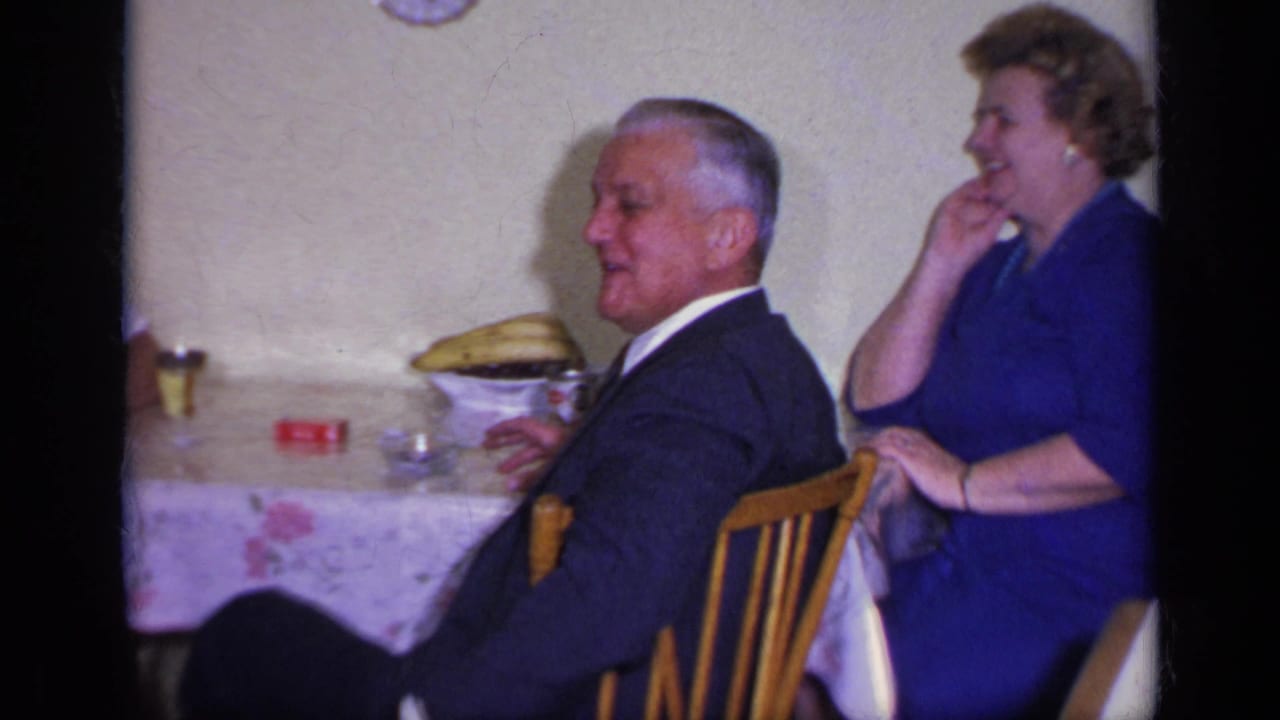 Man in a dark suit and woman in a blue dress seated at a dining table.