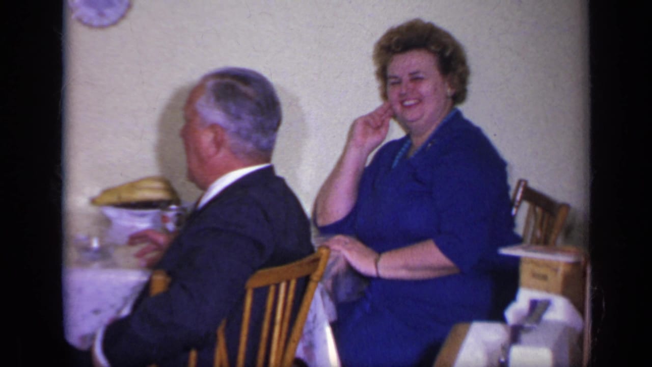 Woman in blue smiles toward the camera while seated behind a man at a table.