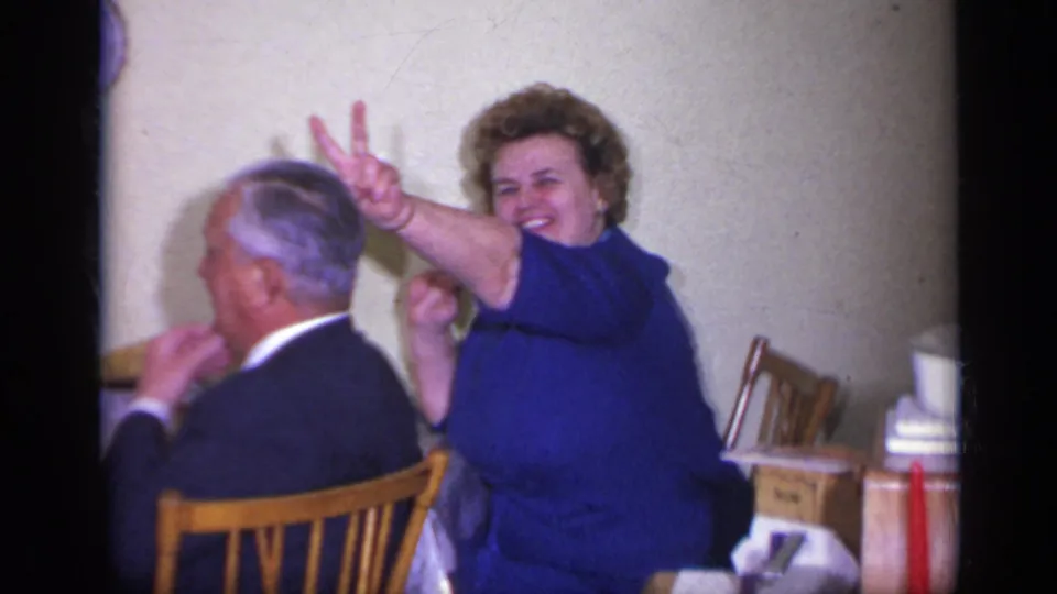 The woman in blue laughs and raises two fingers behind the seated man in this 1969 California dining-room frame.