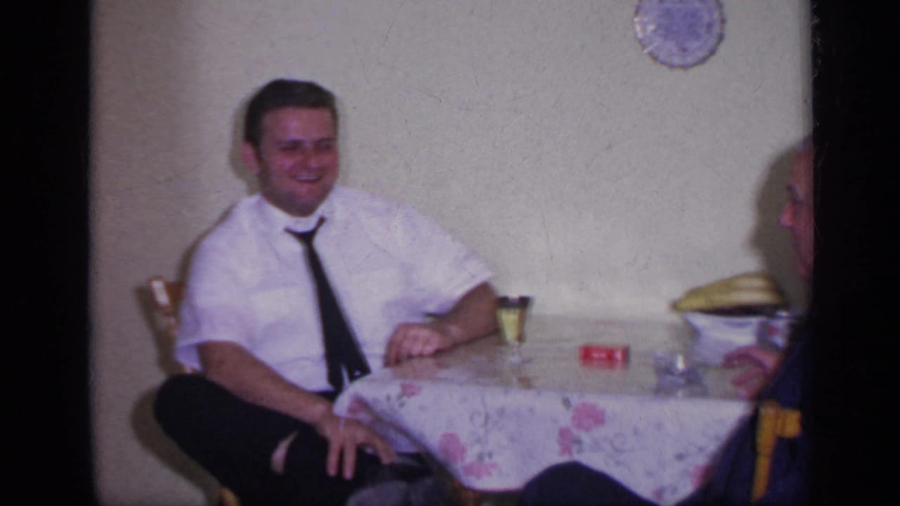 Man in a white shirt and dark tie laughs while seated at a table.