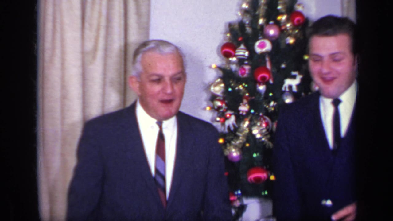 Two adult men in formal suits appear beside a decorated Christmas tree inside a California home in this 1969 8mm frame.
