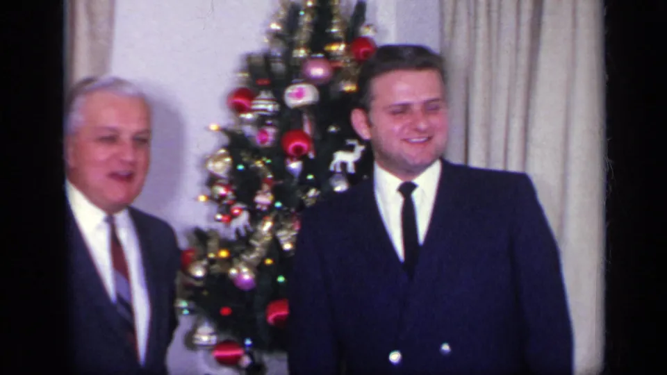 Two suited men appear beside a decorated Christmas tree in a private 1969 California holiday interior.