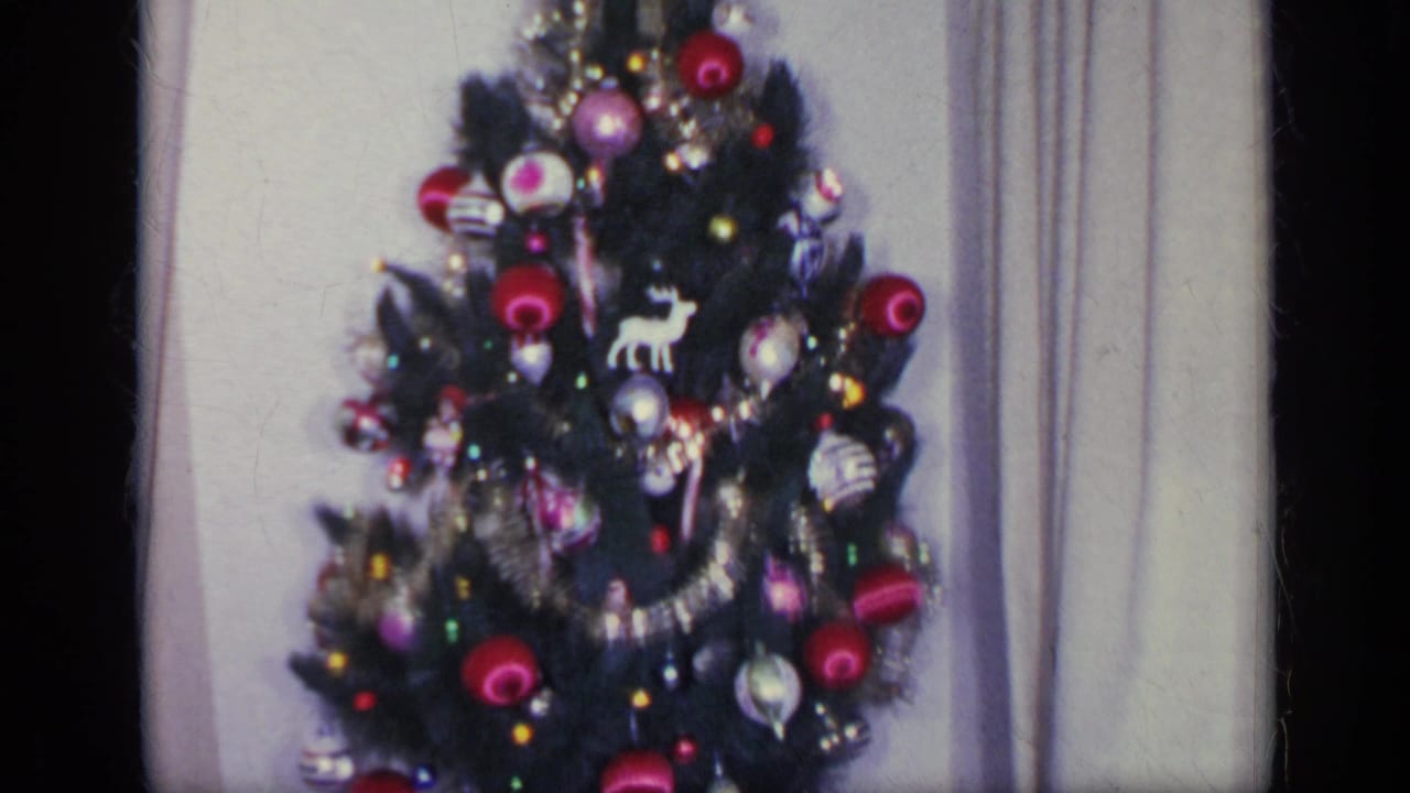 Decorated Christmas tree between curtains with ornaments and tinsel visible.