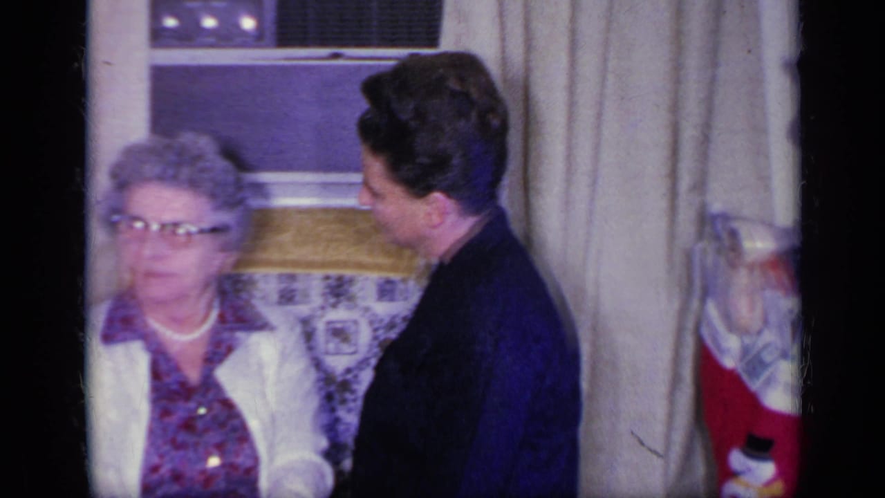 Elderly woman with glasses sits beside a younger woman near a window and Christmas stocking.
