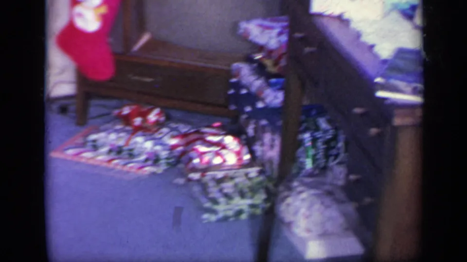 The home-movie frame shows holiday packages spread across a blue carpet near a vintage television and living room furniture.