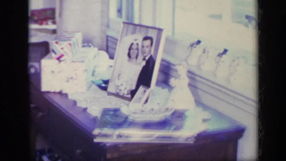 A 1969 California home interior shows a side table with a framed wedding portrait, papers or cards, small objects, and overexposed window light.