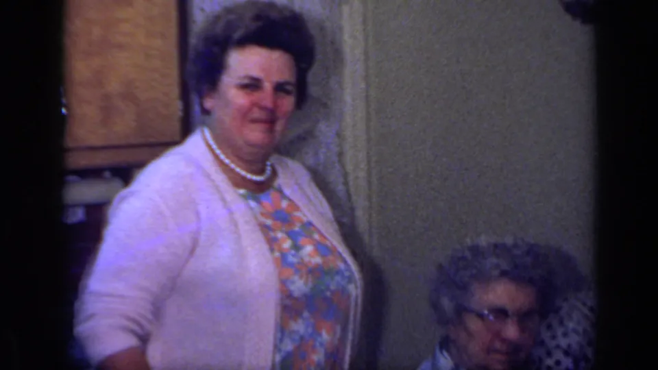 1969 California indoor family gathering with a standing woman in pearls and an older seated woman partly visible.