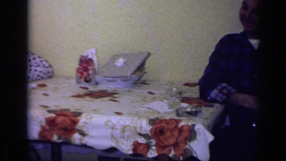 A 1969 California interior shows a dining table with a covered dish, glasses, napkins, and a partially visible adult standing nearby.