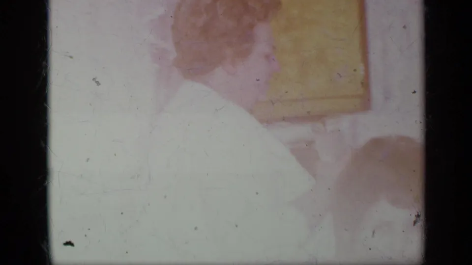A bright, faded 8mm frame shows the woman in profile inside the kitchen, with cabinet shapes and a partial foreground figure visible.