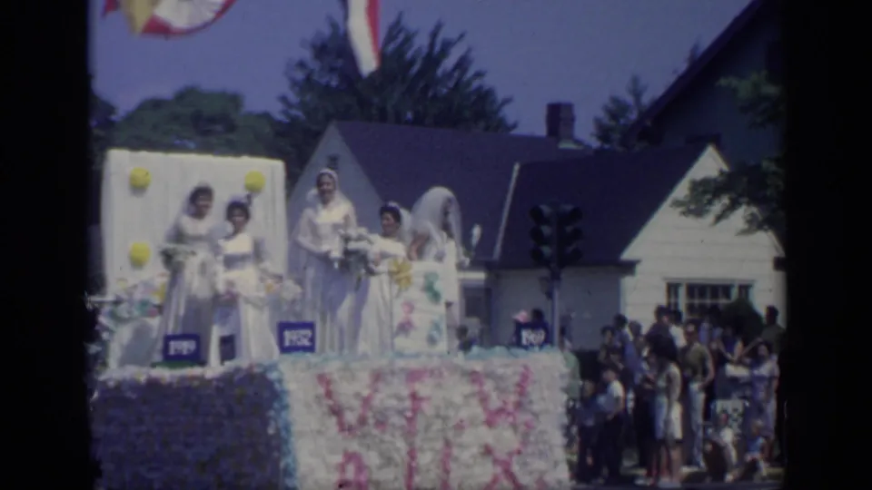A wider 1969 California view shows a bridal-themed float with white drapery, flowers, and spectators gathered beside houses along the parade route.
