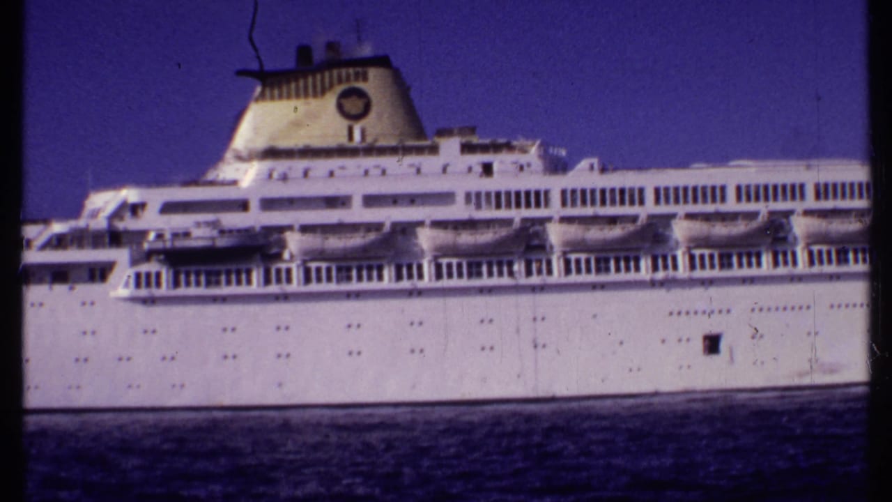 Side view of a white cruise ship with lifeboats and rows of windows.