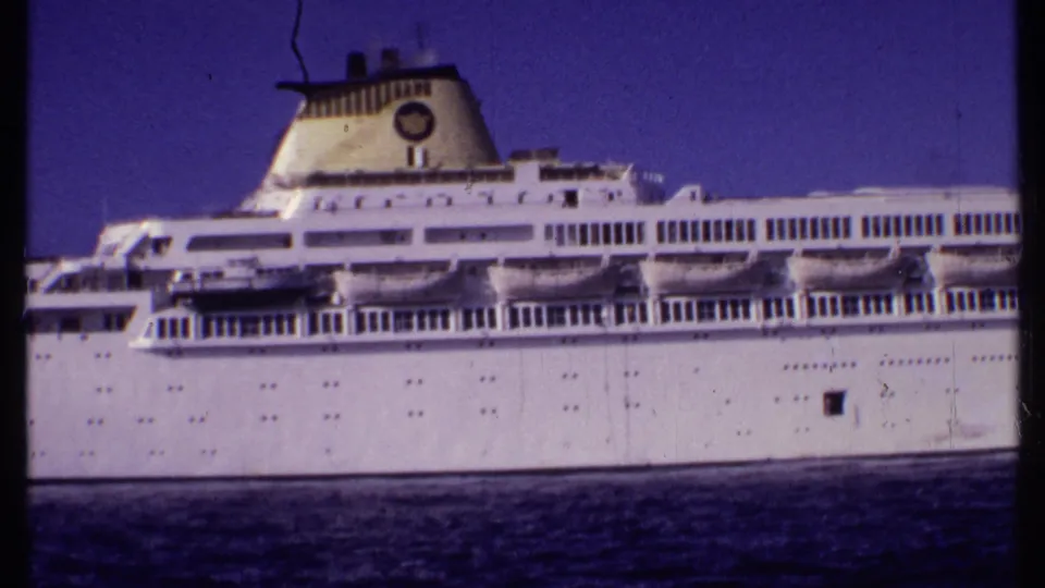1969 Bahamas 8mm frame with a broad side view of a white passenger ship, lifeboats, decks, and calm water.