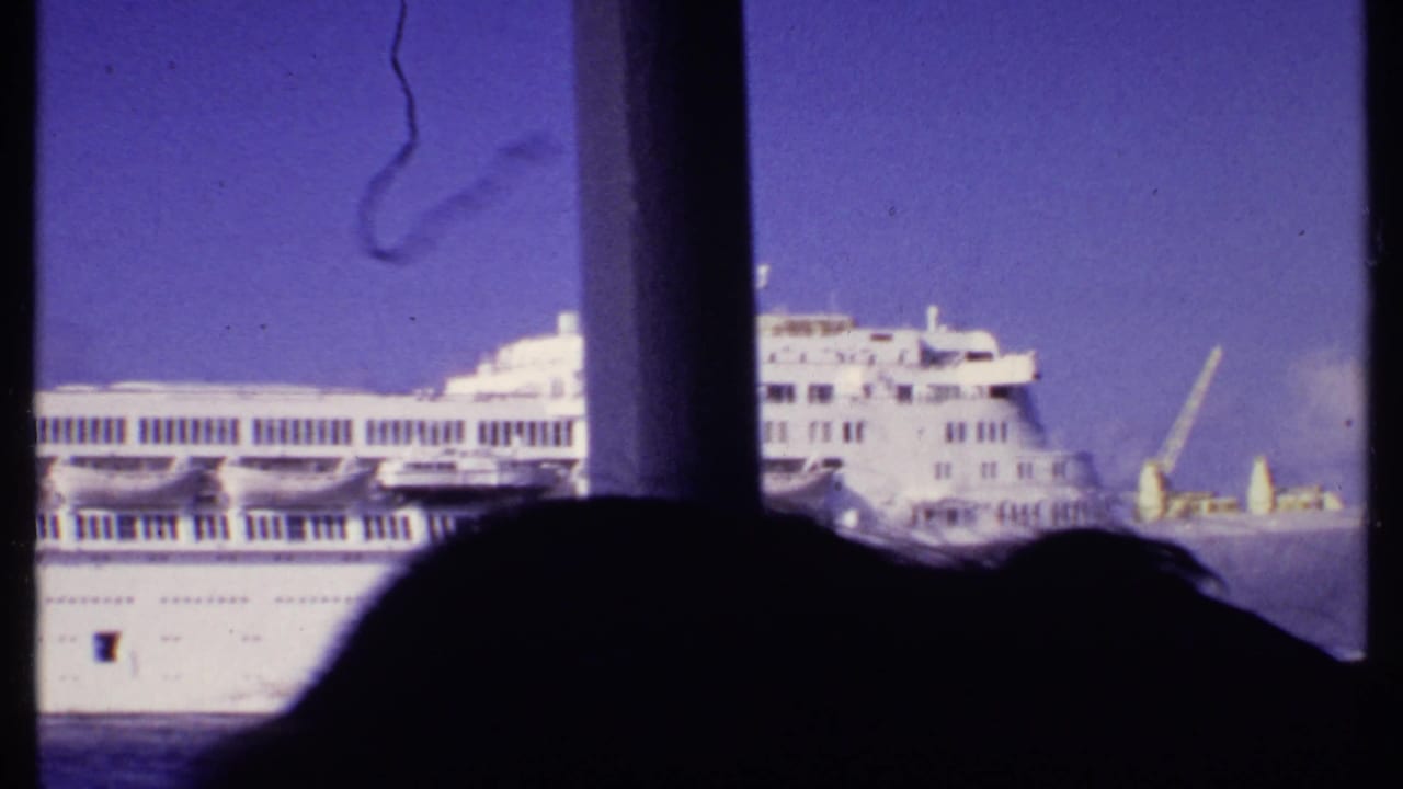 Side of a large white cruise ship with multiple decks on calm water.