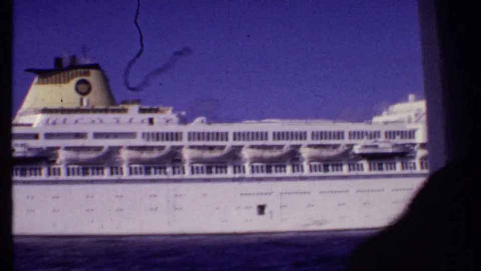 Close 8mm view of the cruise ship's side, showing deck rows and funnel in the metadata-supported Bahamas setting.