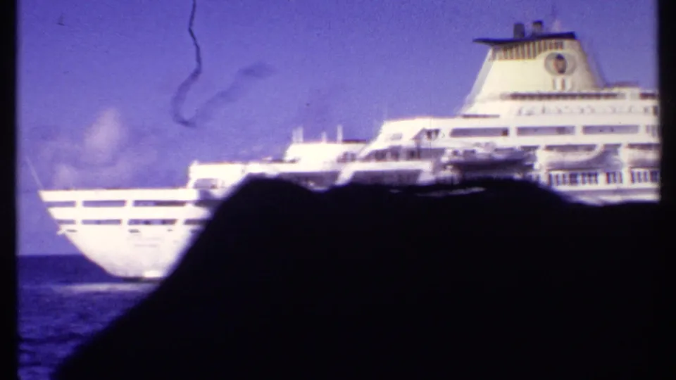1969 Bahamas frame showing the aft portion of a white cruise ship passing beyond a dark passenger silhouette.
