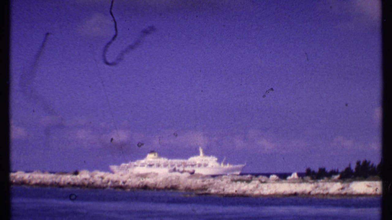 White cruise ship beyond a rocky breakwater with blue water and purple sky.