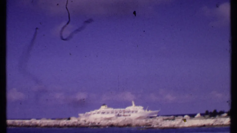 The 8mm frame holds on the cruise ship and breakwater from a shore viewpoint, with soft focus, violet color shift, and visible surface scratches.