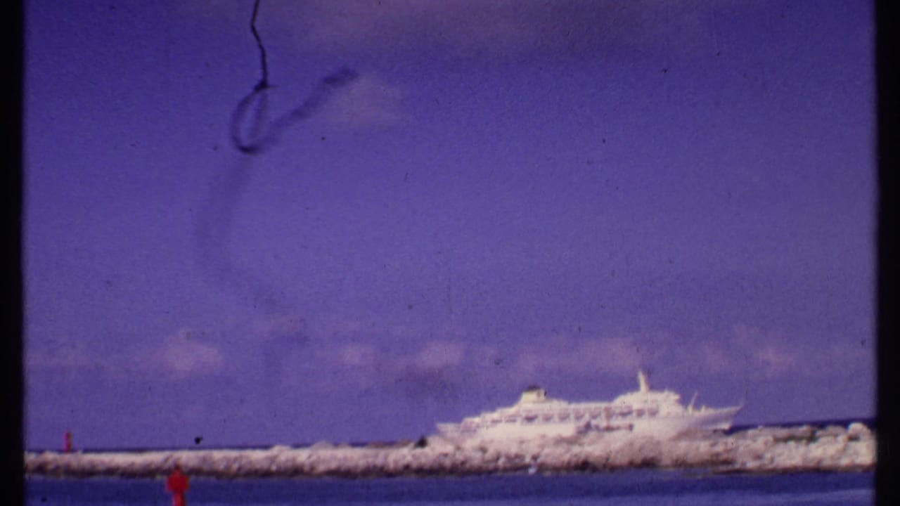 Bahamas 1969 home-movie frame with the cruise ship shifted right of center, a rocky breakwater across the middle, and water in the foreground.