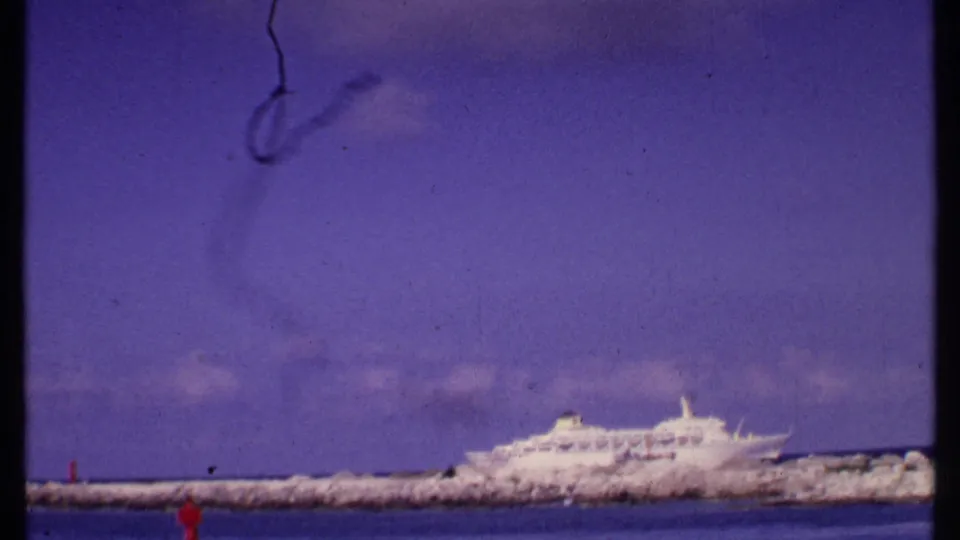 Bahamas 1969 home-movie frame with the cruise ship shifted right of center, a rocky breakwater across the middle, and water in the foreground.