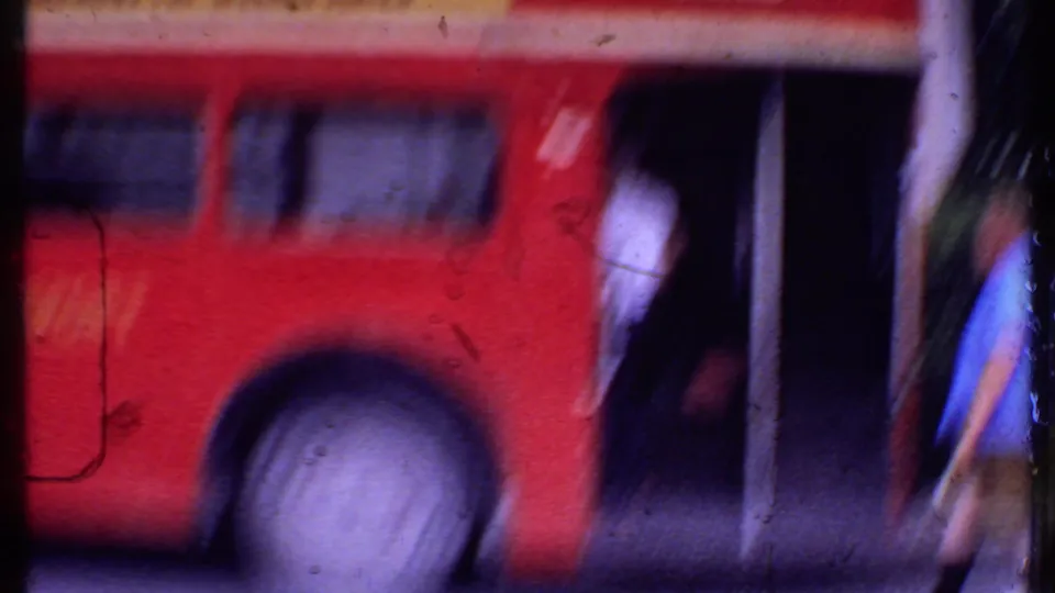 Soft 8mm frame of a red double-decker bus moving or filmed through foreground obstructions in the Bahamas travel sequence.